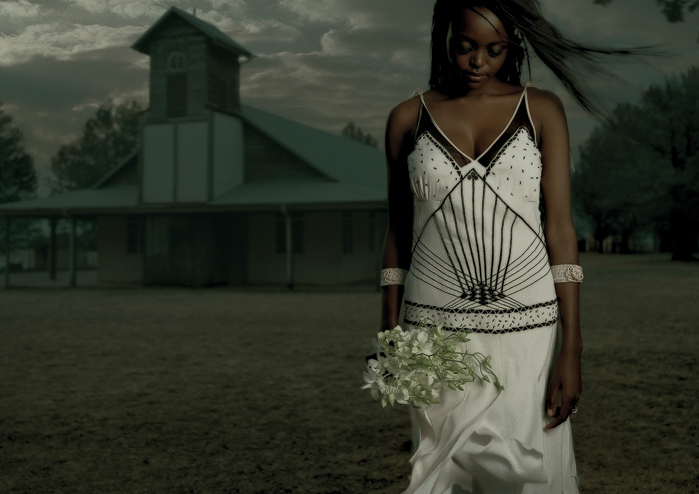 Black bride in beautiful wedding dress holding a bouquet of flowers in front of a church