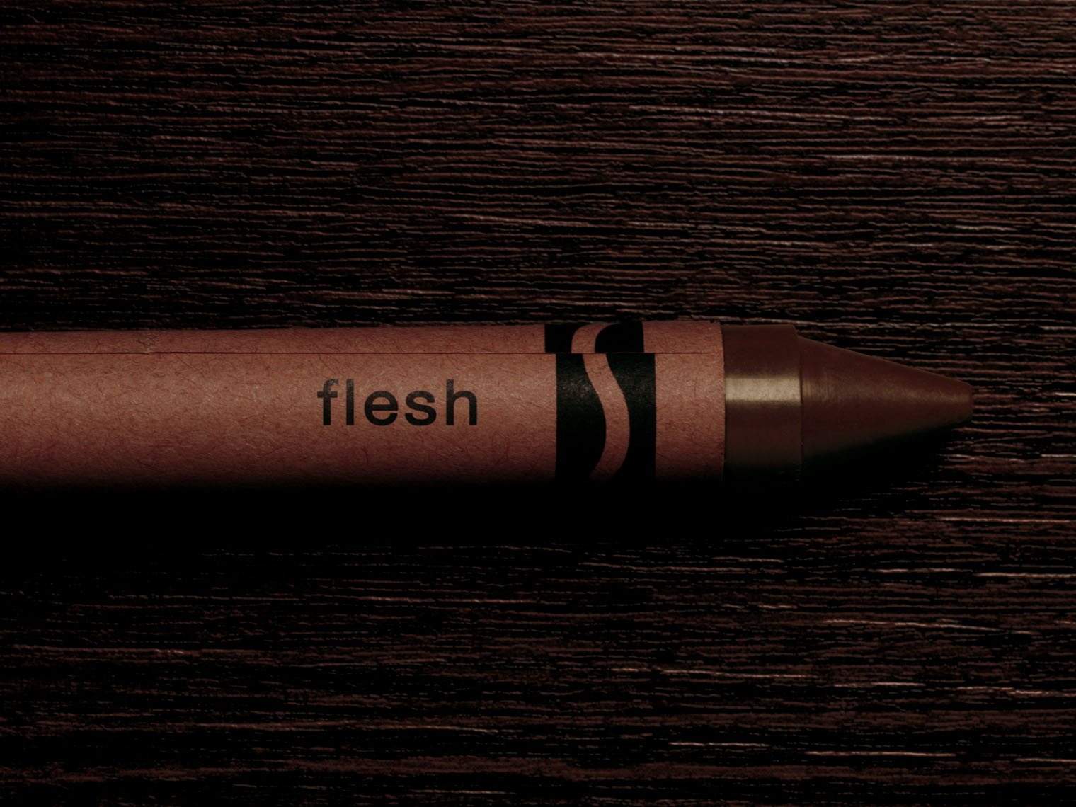 A crayon the colour of black flesh on a dark wooden table. 