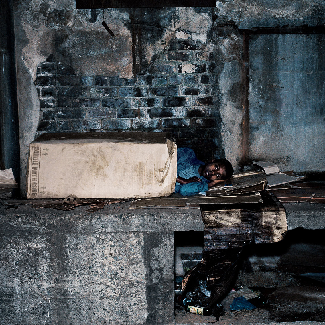 A homeless child sleeping under a cardboard box in a dirty downtown location. 