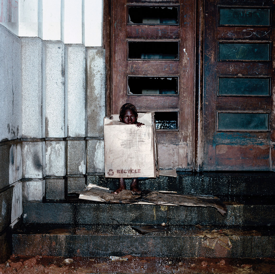Portrait of a homeless child sitting under cardboard boxes to keep warm. 