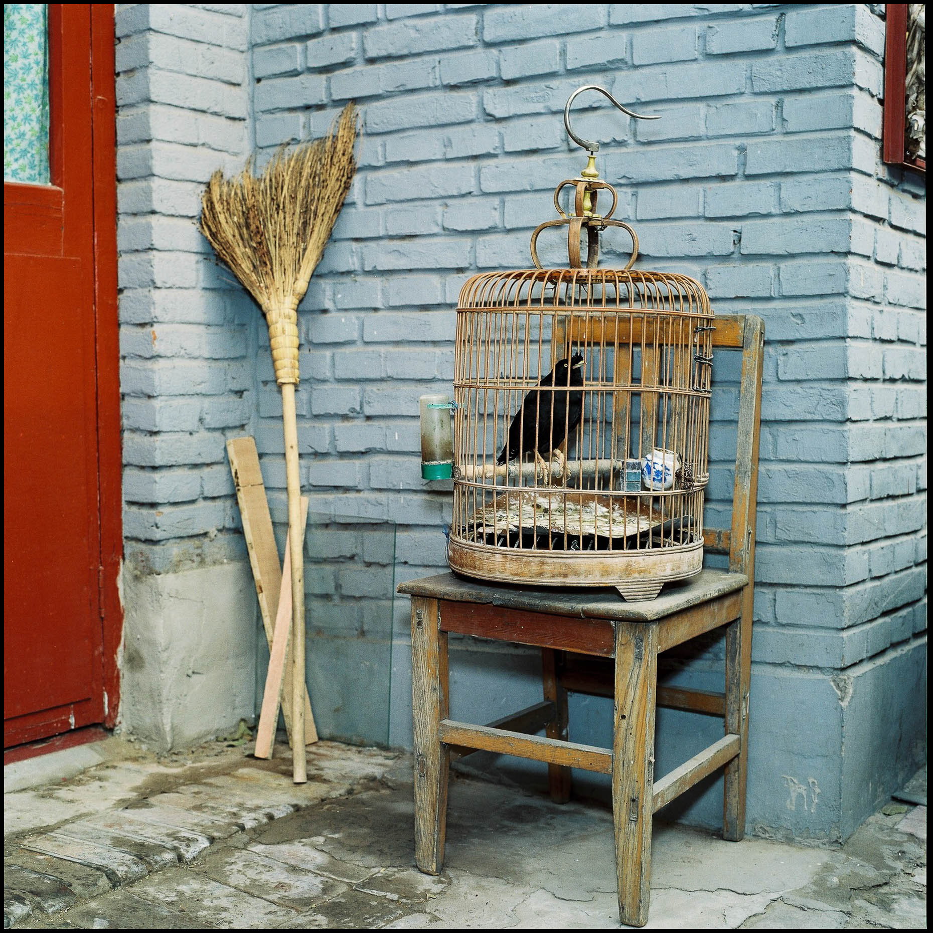 A grass broom and a bird cage outside the front door of a house in the Hutongs, Beijing. 