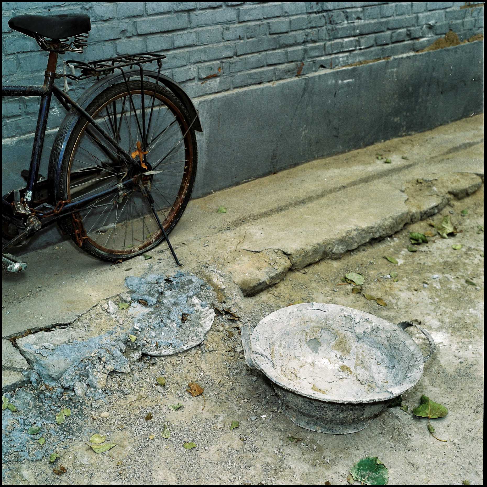 A bicycle, bowl, road and pavement - all in disrepair in the narrow alleys of Beijing. 