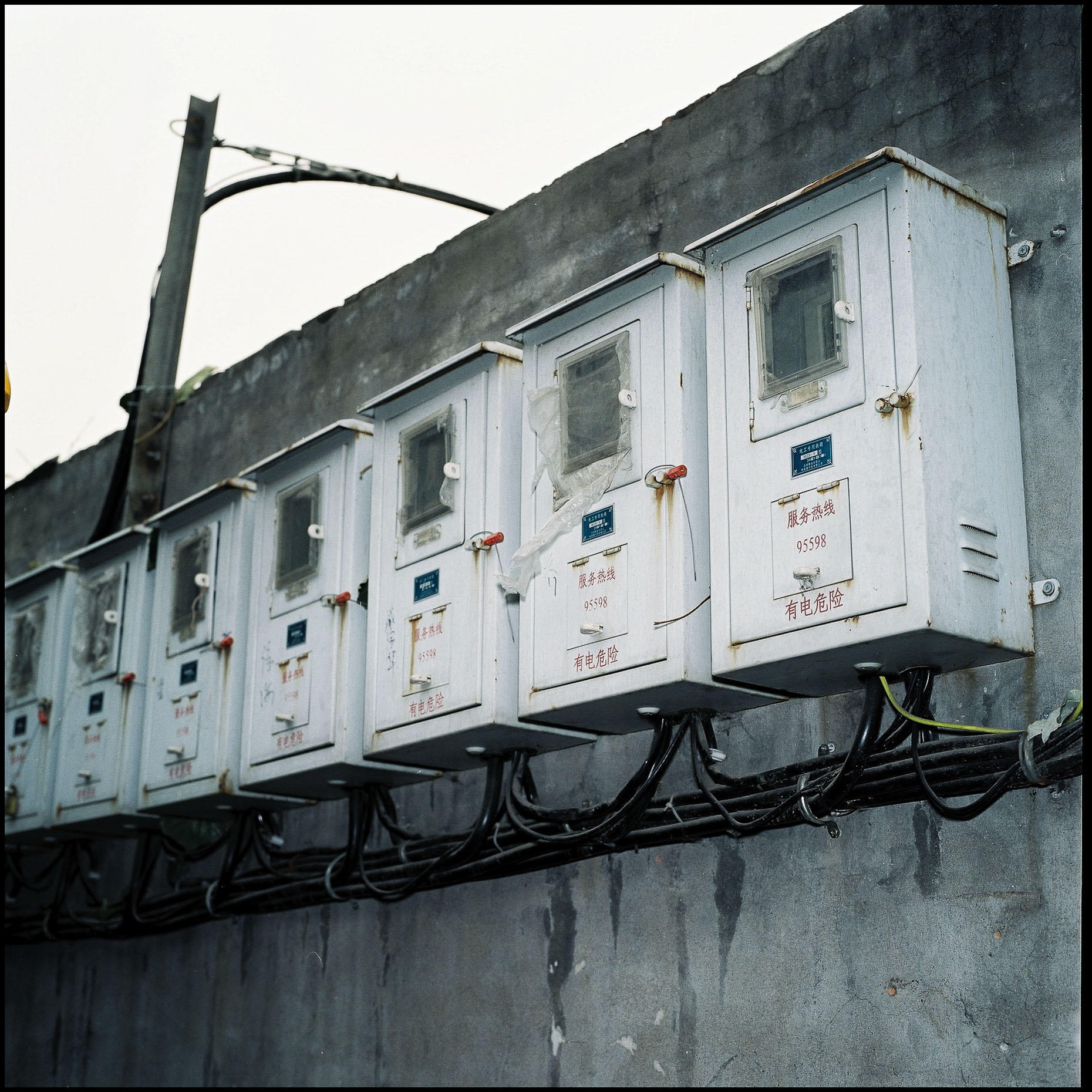 The electricity metres, of all the house in a Hutong,  lined up in a row and mounted on a grey  high wall. 