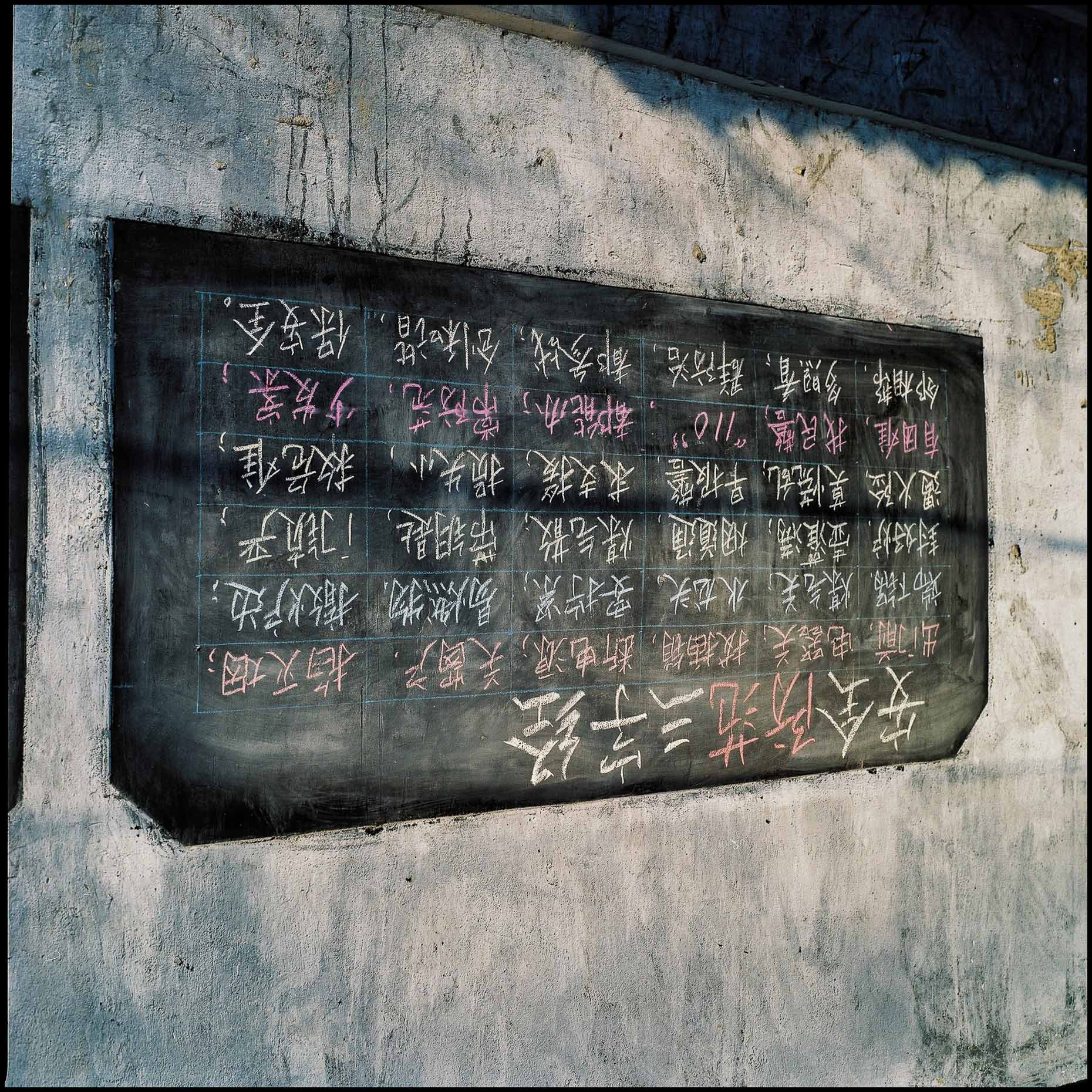 A black board mounted on a wall,  with pink and white chalk chinese writing.  