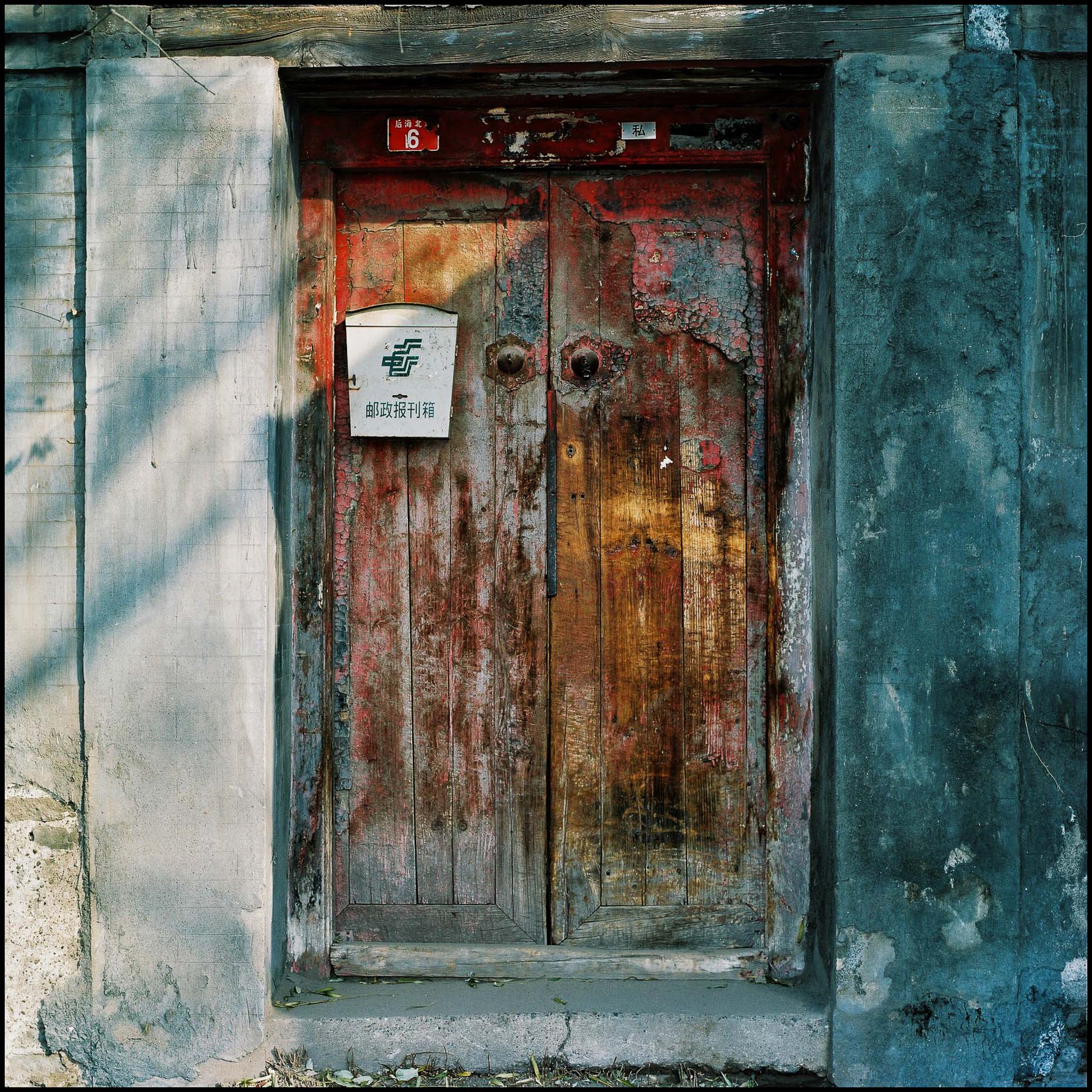 No. 6  a distressed  red wooden door with a  postbox marking the entrance to a courtyard house. 