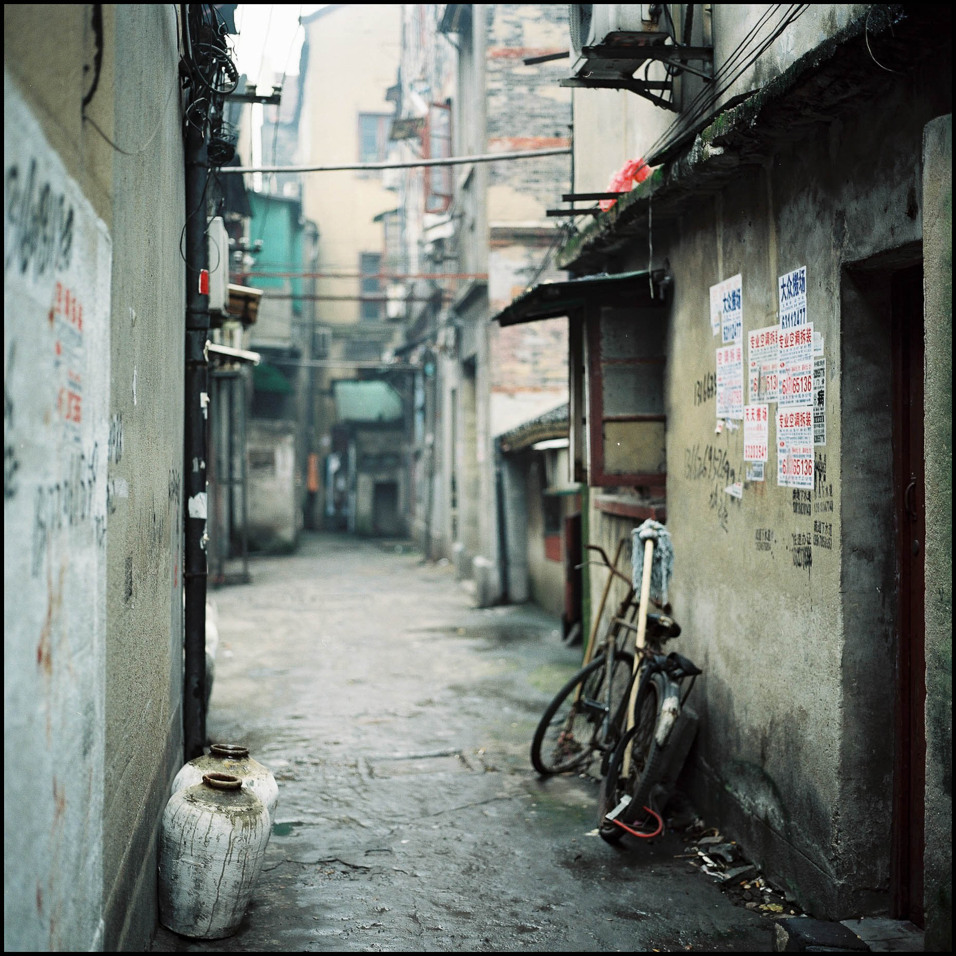 A typical narrow alley with a parked bicycle , rice jars and doorways  leading to various residence or Siheyuans.  
