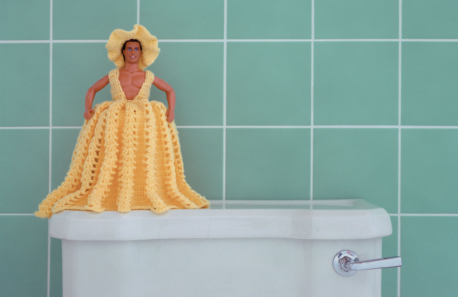 Ken, a toilet holder doll, dressed in a bright yellow crocheted dress and hat.