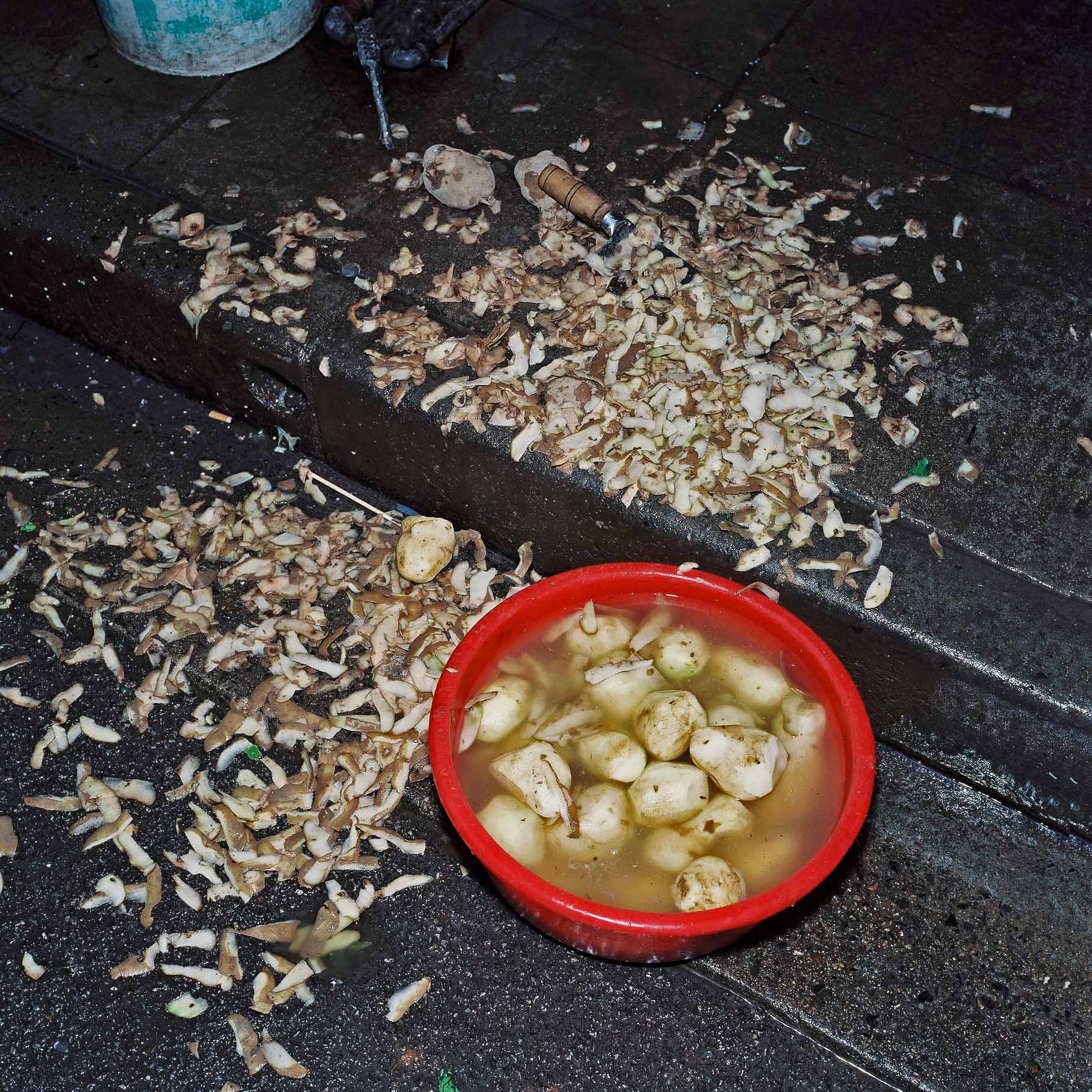 A red plastic bowl with peeled potatoes and peelings scattered around. 