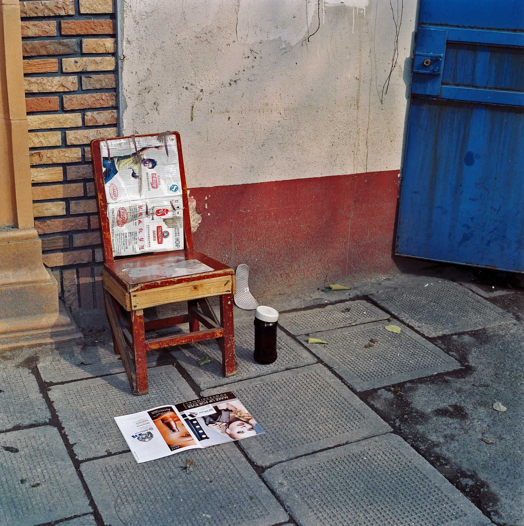 A  red chair,  tea flask and magazine on the sidewalk. 