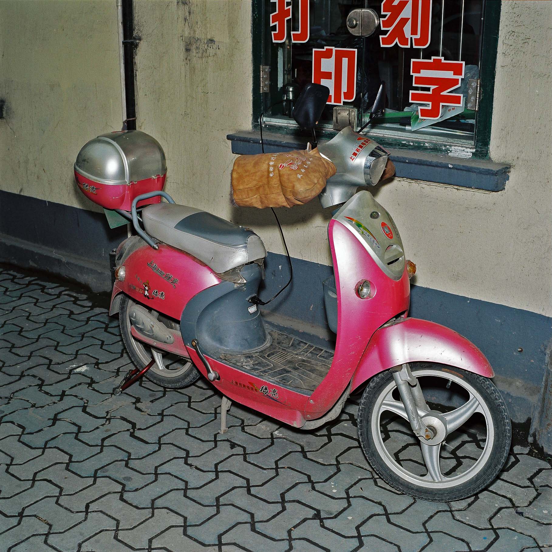 A red scooter parked in front of a window with red Chinese writing. 