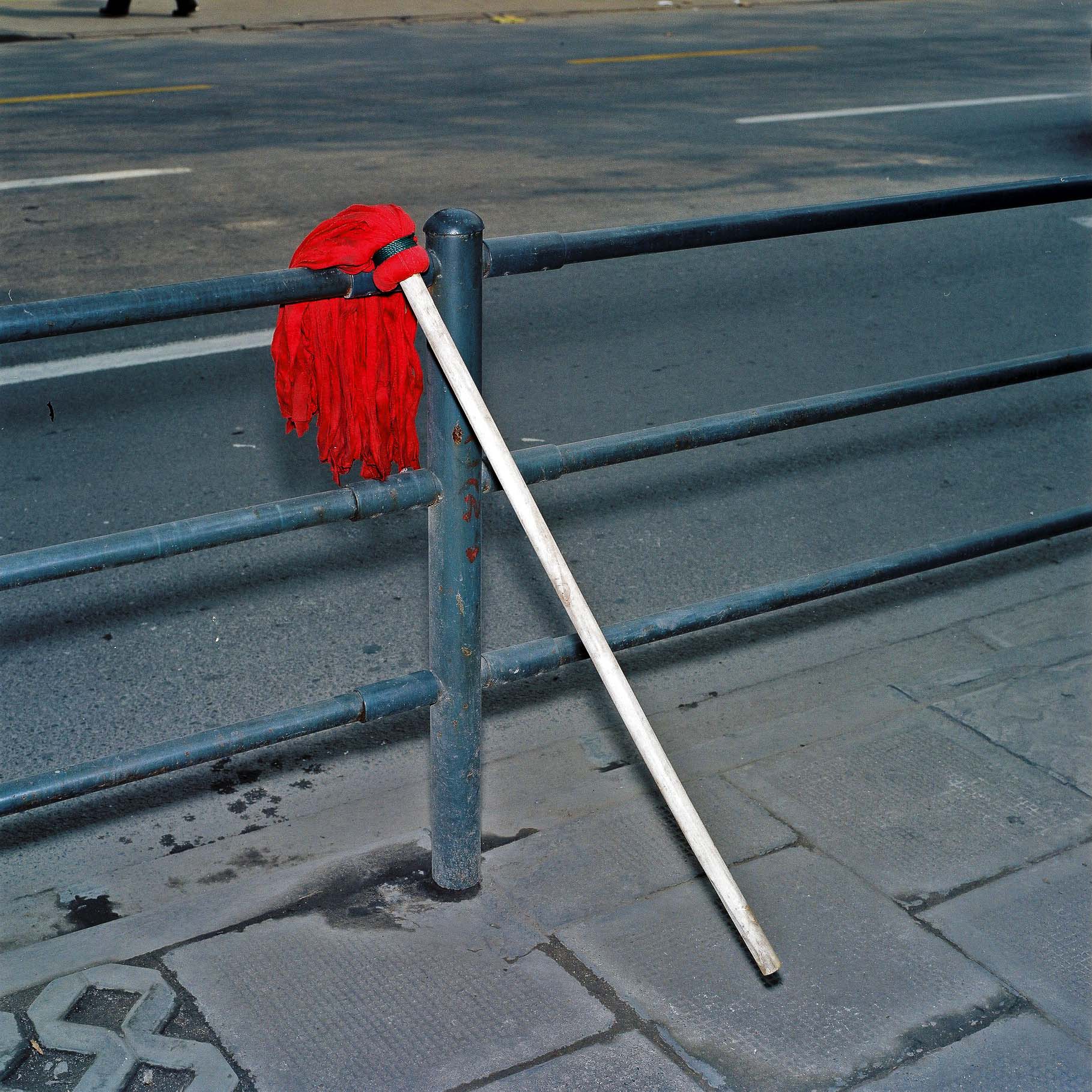 A red mop drying on a street railing. 