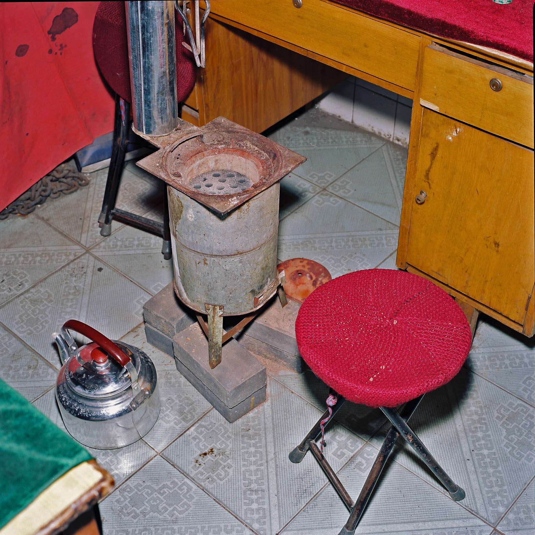 A tri-pod chair with a red crochet covering in front of a coal burner.