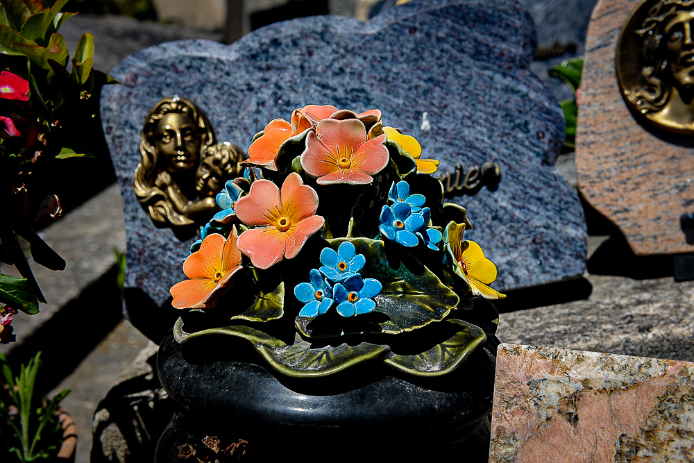 An orange, blue and yellow  immortelle  grave ornament amongst the graves of the deceased . 