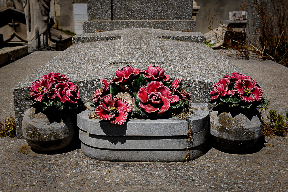 One big and two smaller, pink rose,  grave decorations placed at the foot of an overgrown  grave. 