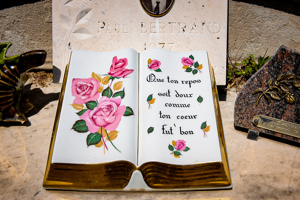 An open gold and white ceramic ,grave decoration book, the open pages decorated with pink roses and a written verse. 
