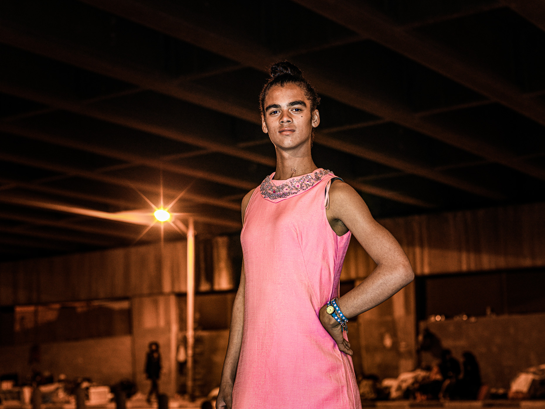 A trans woman, dress classically in pink,  posing to have her portrait taken. 
