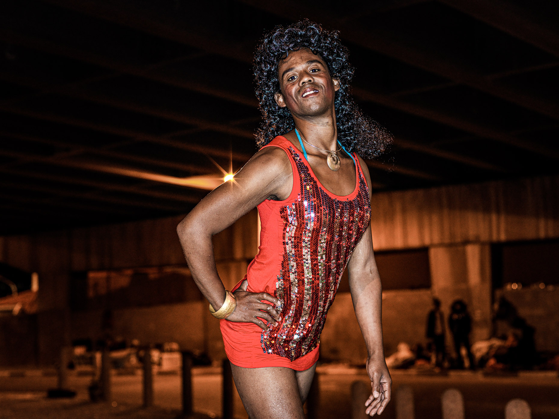 A trans woman dressed in a red mini dress,  posing to have her portrait taken.