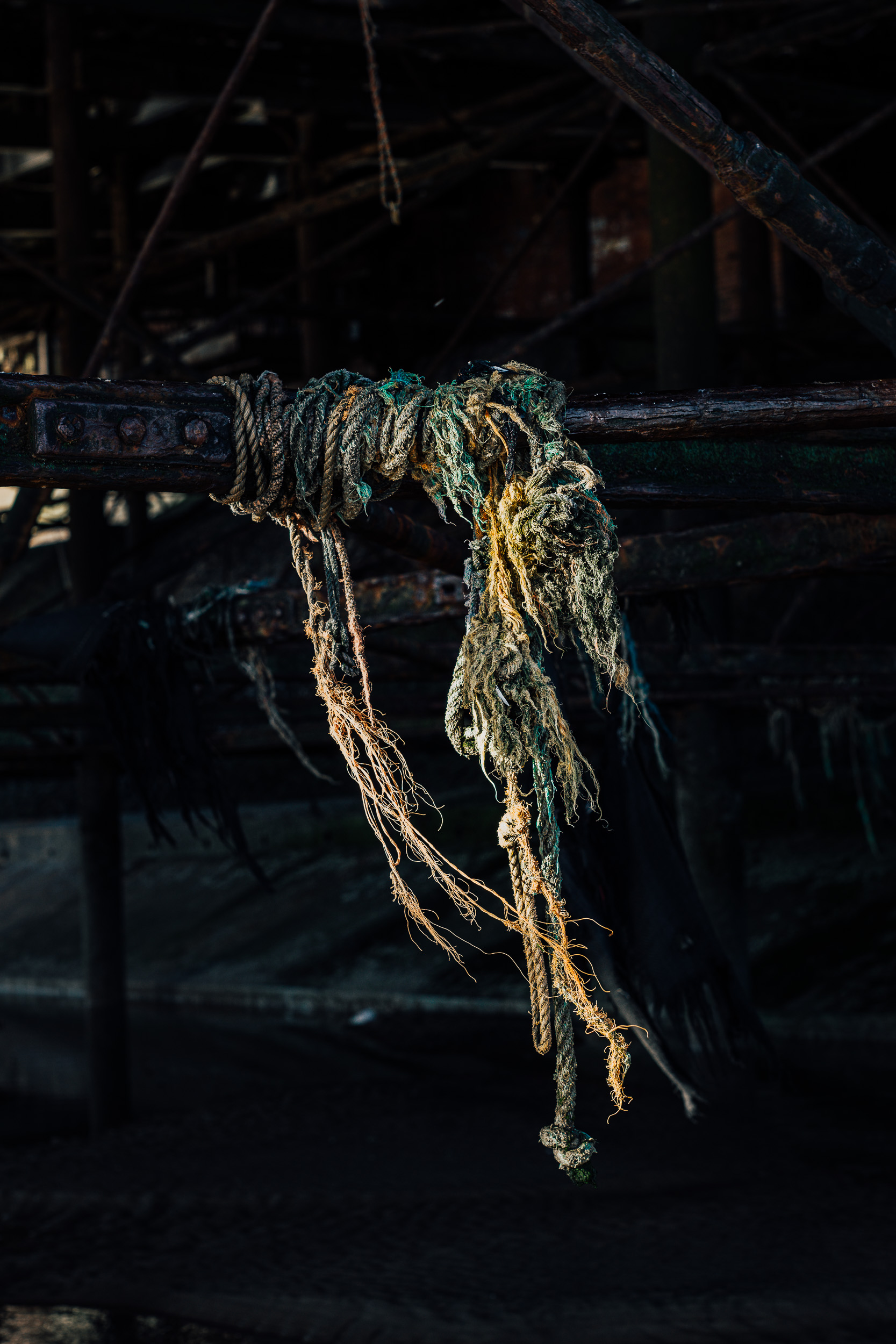 A cluster of  abandoned rope and fishing nets, blown by a gentle breeze and dangling off a steel railing. 